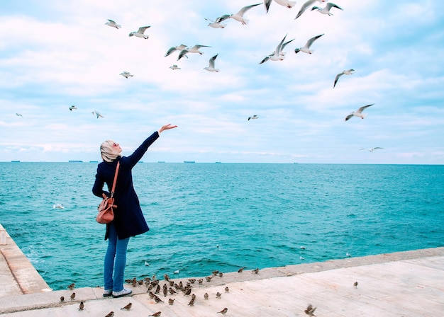 blonde woman feeding seagulls in cloudy autumn day on the sea coast