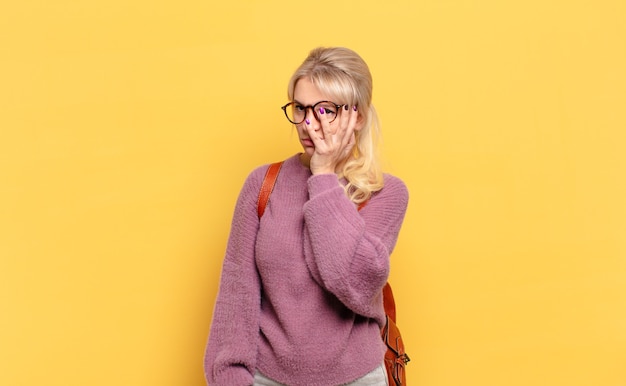 Blonde woman feeling bored, frustrated and sleepy after a tiresome, dull and tedious task, holding face with hand