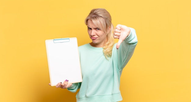 Blonde woman feeling cross, angry, annoyed, disappointed or displeased, showing thumbs down with a serious look