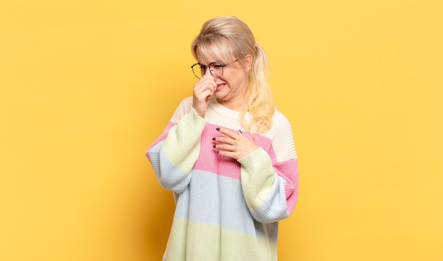 Blonde woman feeling disgusted, holding nose to avoid smelling a foul and unpleasant stench