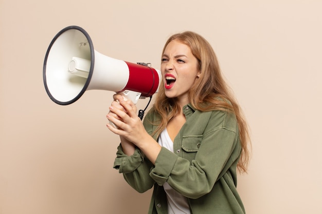 Blonde woman feeling happy, excited and positive, giving a big shout out with hands next to mouth, calling out