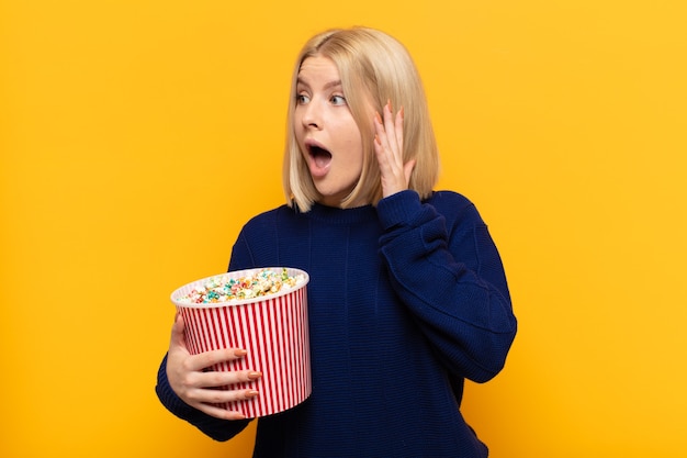 Blonde woman feeling happy, excited and surprised, looking to the side with both hands on face