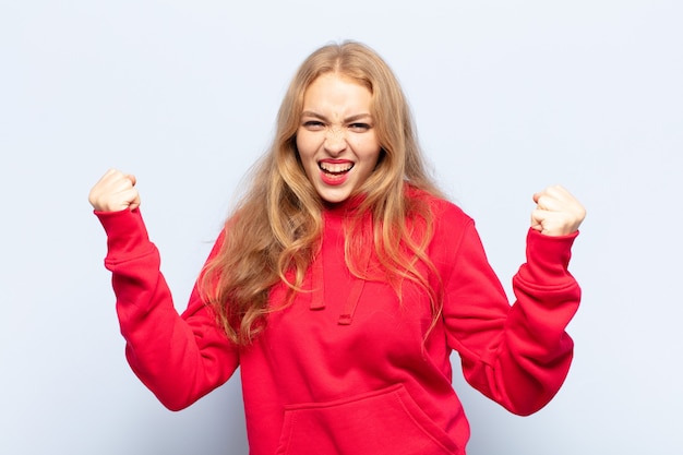 Blonde woman feeling happy, positive and successful, celebrating victory, achievements or good luck