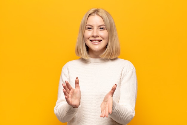 Blonde woman feeling happy and successful, smiling and clapping hands, saying congratulations with an applause