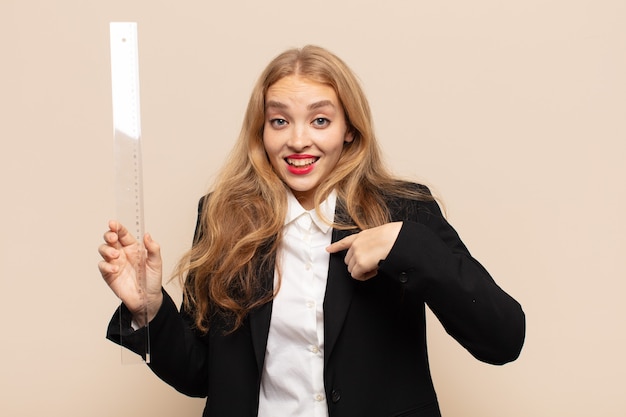 Blonde woman feeling happy, surprised and proud, pointing to self with an excited, amazed look