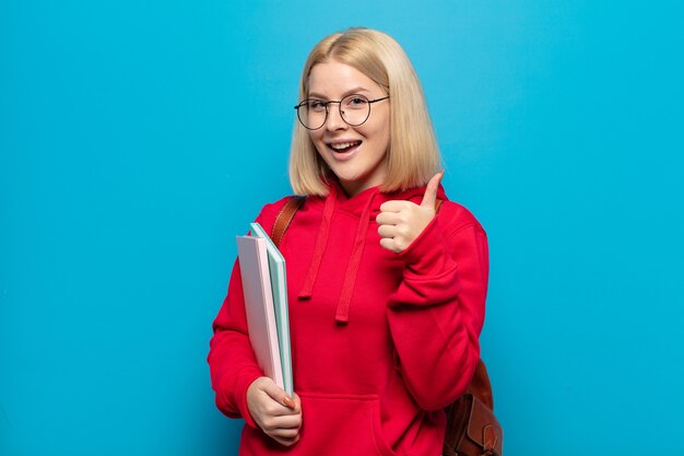 Blonde woman feeling proud, carefree, confident and happy, smiling positively with thumbs up