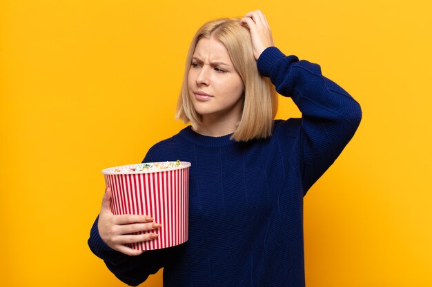 Donna bionda che si sente perplessa e confusa, grattandosi la testa e guardando di lato