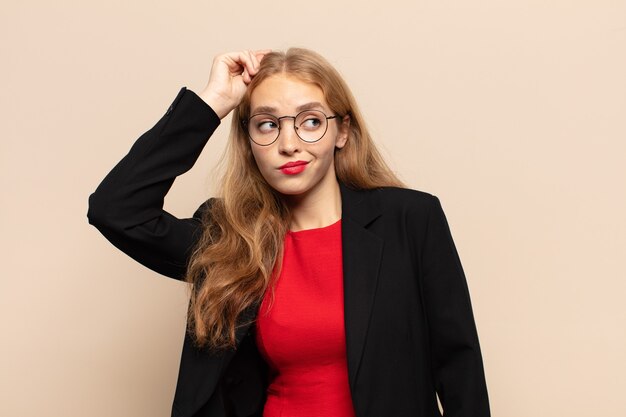 Blonde woman feeling puzzled and confused, scratching head and looking to the side