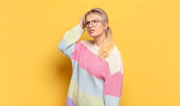 Blonde woman feeling puzzled and confused, scratching head and looking to the side