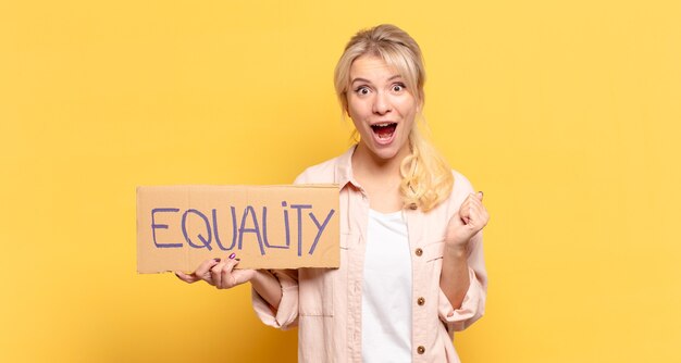 Blonde woman feeling shocked, excited and happy, laughing and celebrating success, saying wow!