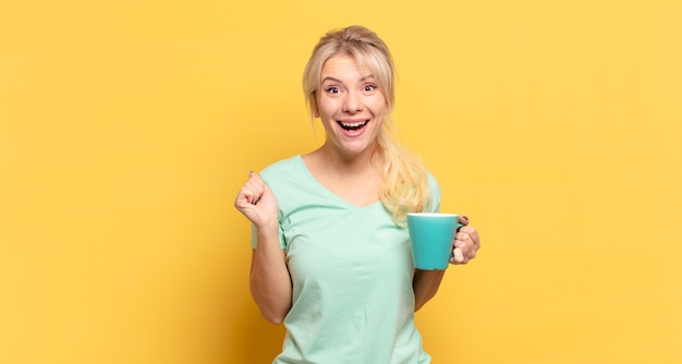 Blonde woman feeling shocked, excited and happy, laughing and celebrating success, saying wow!