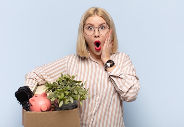 Photo blonde woman feeling shocked and scared, looking terrified with open mouth and hands on cheeks