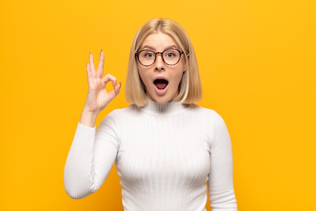 blonde woman feeling successful and satisfied, smiling with mouth wide open, making okay sign with hand