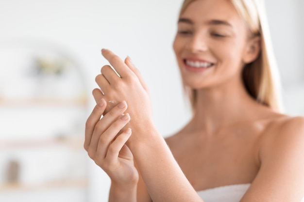 Photo blonde woman gently rubbing moisturizer on her hands in bathroom