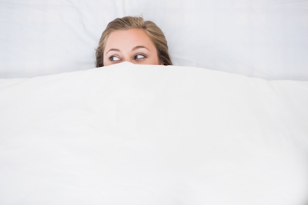 Блондинка женщина прячется под одеялом