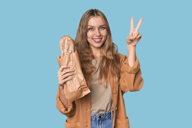 Блондинка с хлебом в студии, показывающая номер два пальцами