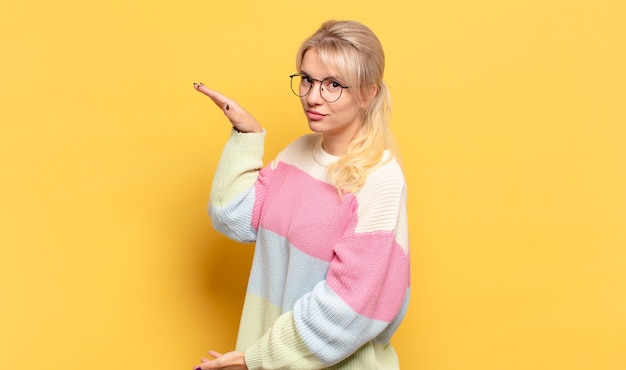 Блондинка женщина держит объект обеими руками на боковой копии пространства, показывая, предлагая или рекламируя объект
