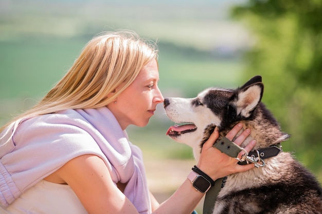 Blonde woman hugging her furry friend siberian husky on the background of a forest road on a sunny day