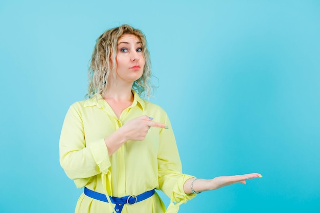 Blonde woman is raising up her handful and showing it with forefinger on blue background