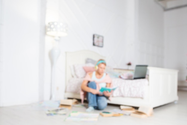 Photo a blonde woman is sitting near the bed with a laptop and headphones