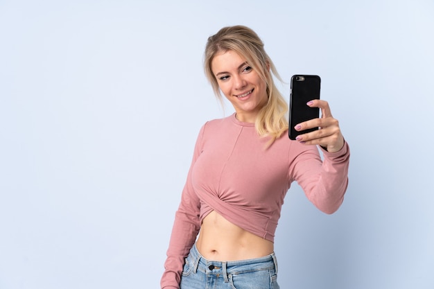 Blonde woman over isolated blue  making a selfie