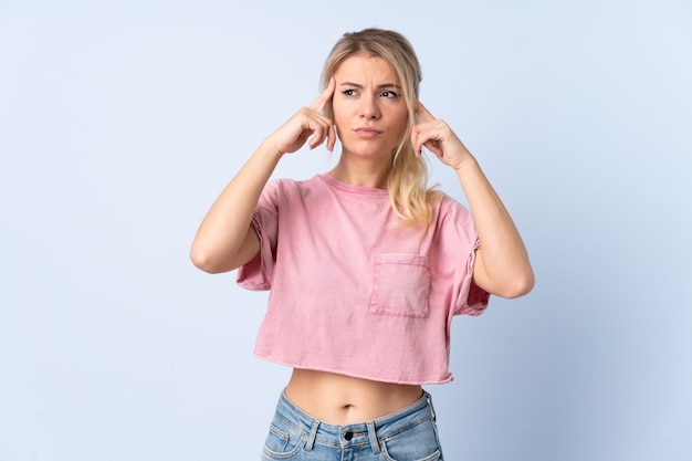 Blonde woman over isolated blue wall having doubts and thinking