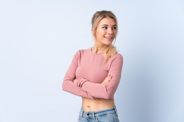 Blonde woman over isolated blue  with arms crossed and happy