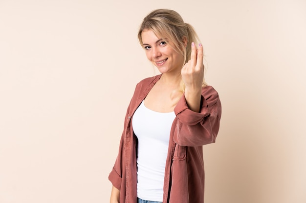 Blonde woman over isolated wall making money gesture
