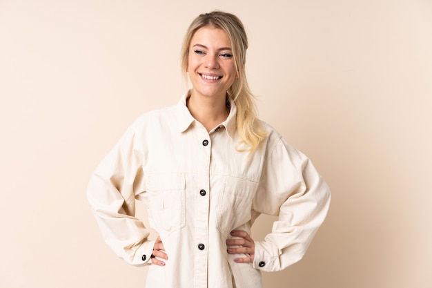 Blonde woman over isolated wall posing with arms at hip and smiling