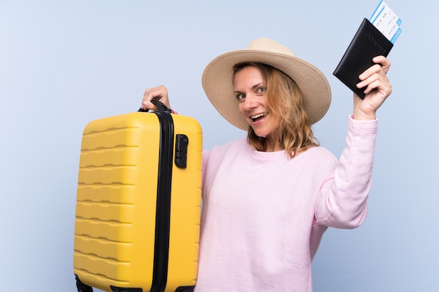 スーツケースとパスポートで休暇に孤立した壁の上の金髪の女性