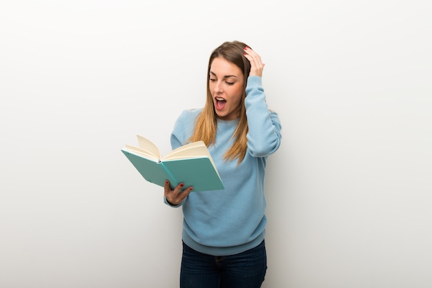 Donna bionda su sfondo bianco isolato sorpreso mentre godendo la lettura di un libro