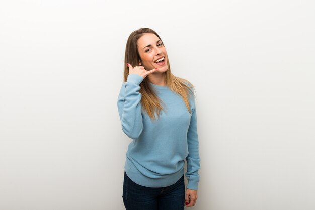 Blonde woman on isolated white wall making phone gesture. Call me back sign