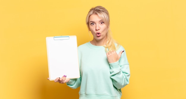 Blonde woman looking astonished in disbelief, pointing at object on the side and saying wow, unbelievable