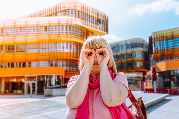 blonde woman looking at camera through an imaginary spyglass against backdrop of architecture