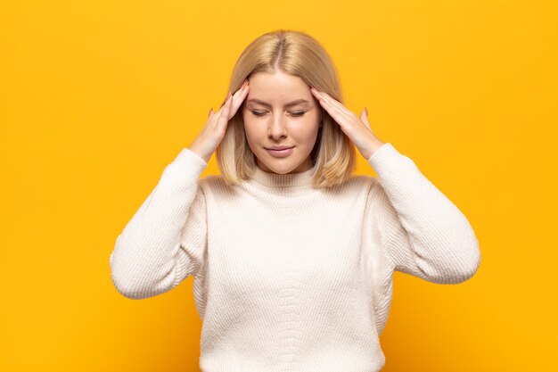 Blonde woman looking concentrated, thoughtful and inspired, brainstorming and imagining with hands on forehead