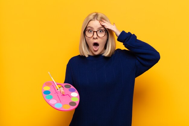 Blonde woman looking happy, astonished and surprised, smiling and realizing amazing and incredible good news