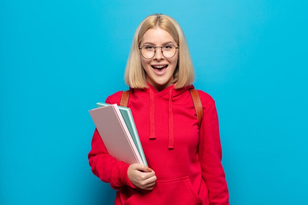 Blonde woman looking happy and pleasantly surprised, excited with a fascinated and shocked expression