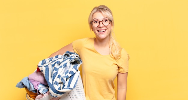 Blonde woman looking happy and pleasantly surprised, excited with a fascinated and shocked expression