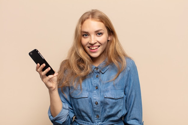 Blonde woman looking happy and pleasantly surprised, excited with a fascinated and shocked expression