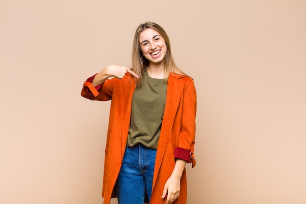 Blonde woman looking happy, proud and surprised, cheerfully pointing to self, feeling confident and lofty