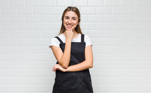 Donna bionda che sembra felice e sorridente con la mano sul mento, chiedendosi o facendo una domanda, confrontando le opzioni