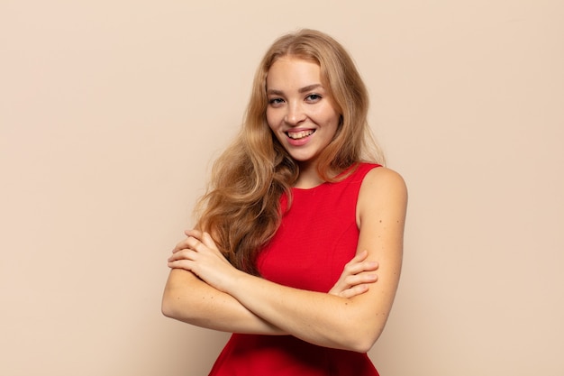 blonde woman looking like a happy, proud and satisfied achiever smiling with arms crossed