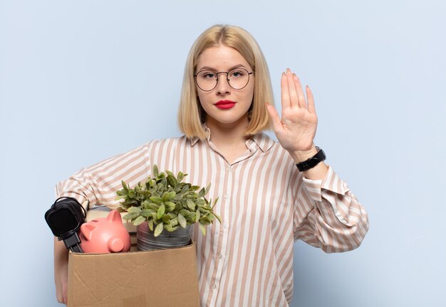 Blonde woman looking serious, stern, displeased and angry showing open palm making stop gesture