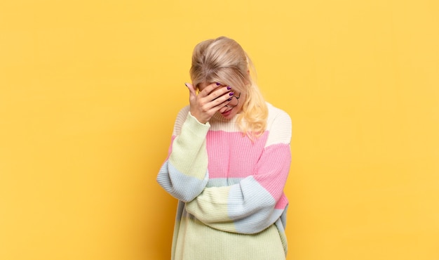 Blonde woman looking stressed, ashamed or upset, with a headache, covering face with hand