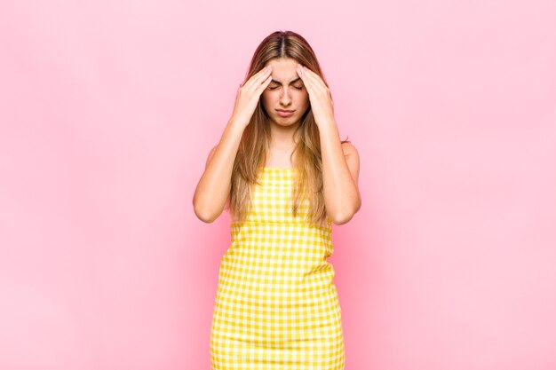 Blonde woman looking stressed and frustrated, working under pressure with a headache and troubled with problems