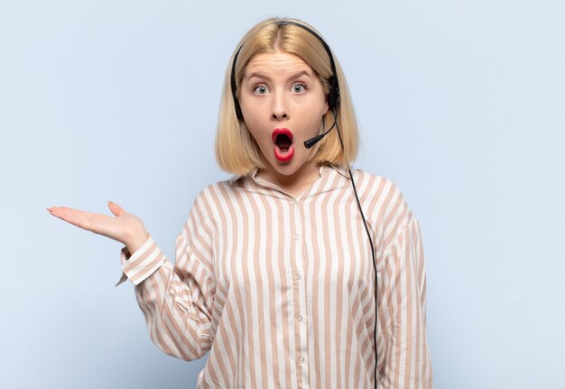 Blonde woman looking surprised and shocked, with jaw dropped holding an object with an open hand on the side