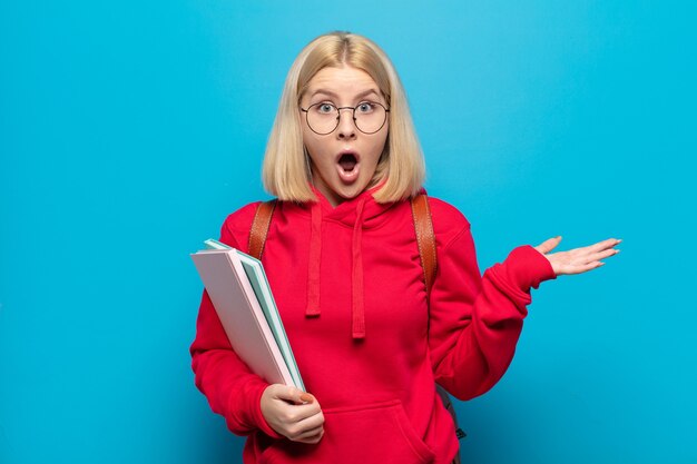 Blonde woman looking surprised and shocked, with jaw dropped holding an object with an open hand on the side