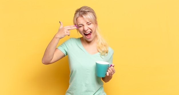 Blonde woman looking unhappy and stressed, suicide gesture making gun sign with hand, pointing to head