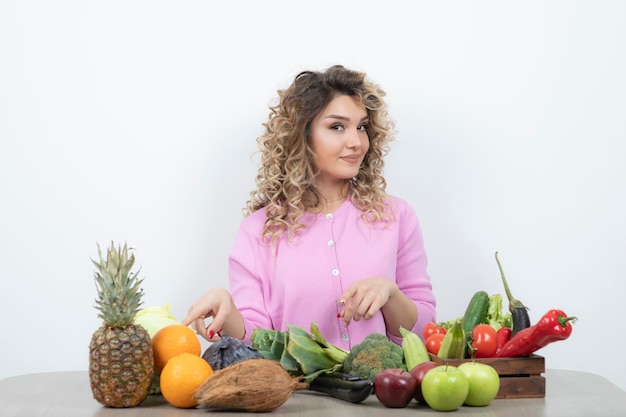 blonde woman in pink top sitting at table with many fruits.