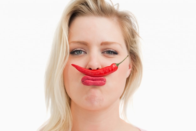 Blonde woman placing a chili between her nose and her mouth